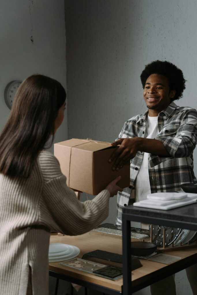 A young man hands over a package to a woman in an indoor setting, symbolizing delivery services.