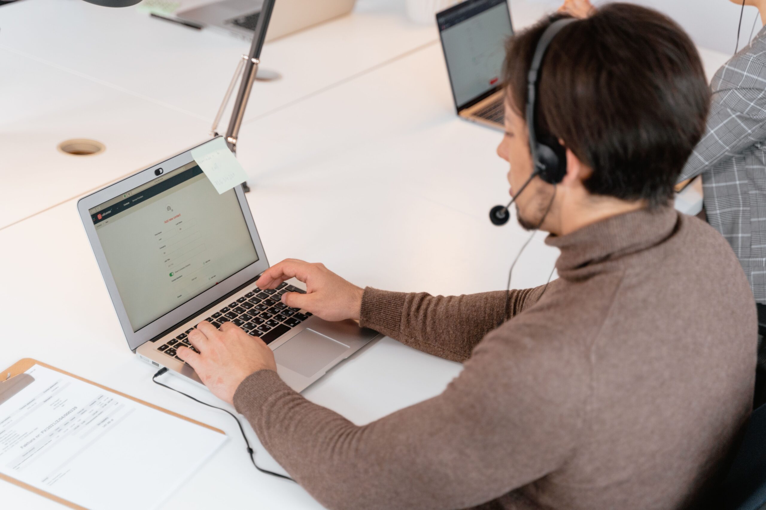 pexels photo 7709171 7709171 Call center agent wearing headphones working on a laptop in a modern office setting.